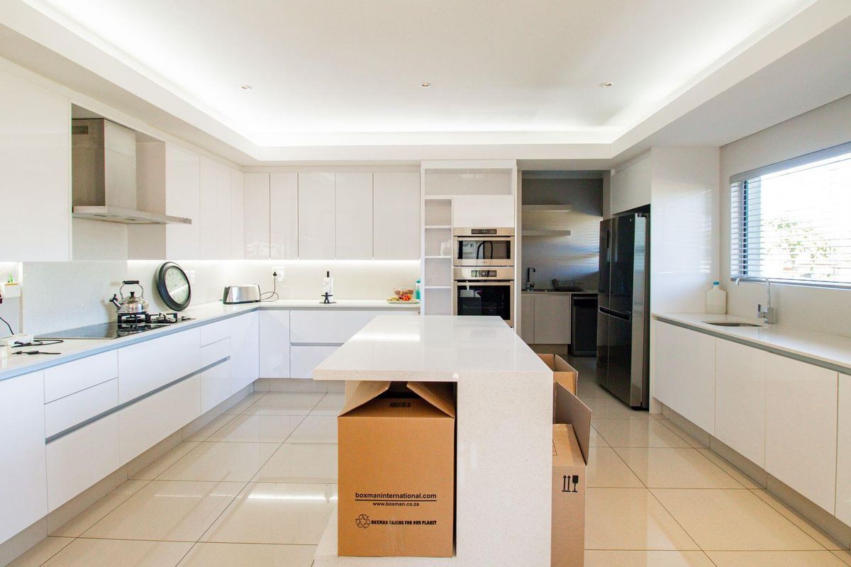 Modern, spacious kitchen featuring high-gloss cabinetry, stone countertops, a central island, integrated oven and microwave, and a separate scullery area.