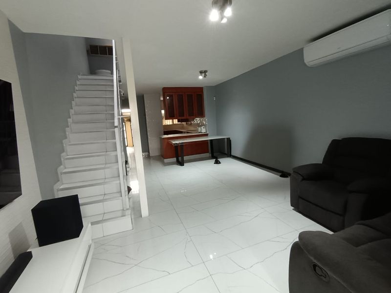 Open-plan living area featuring modern white tiled flooring, a staircase, and a kitchen with wooden cabinetry and a breakfast bar.