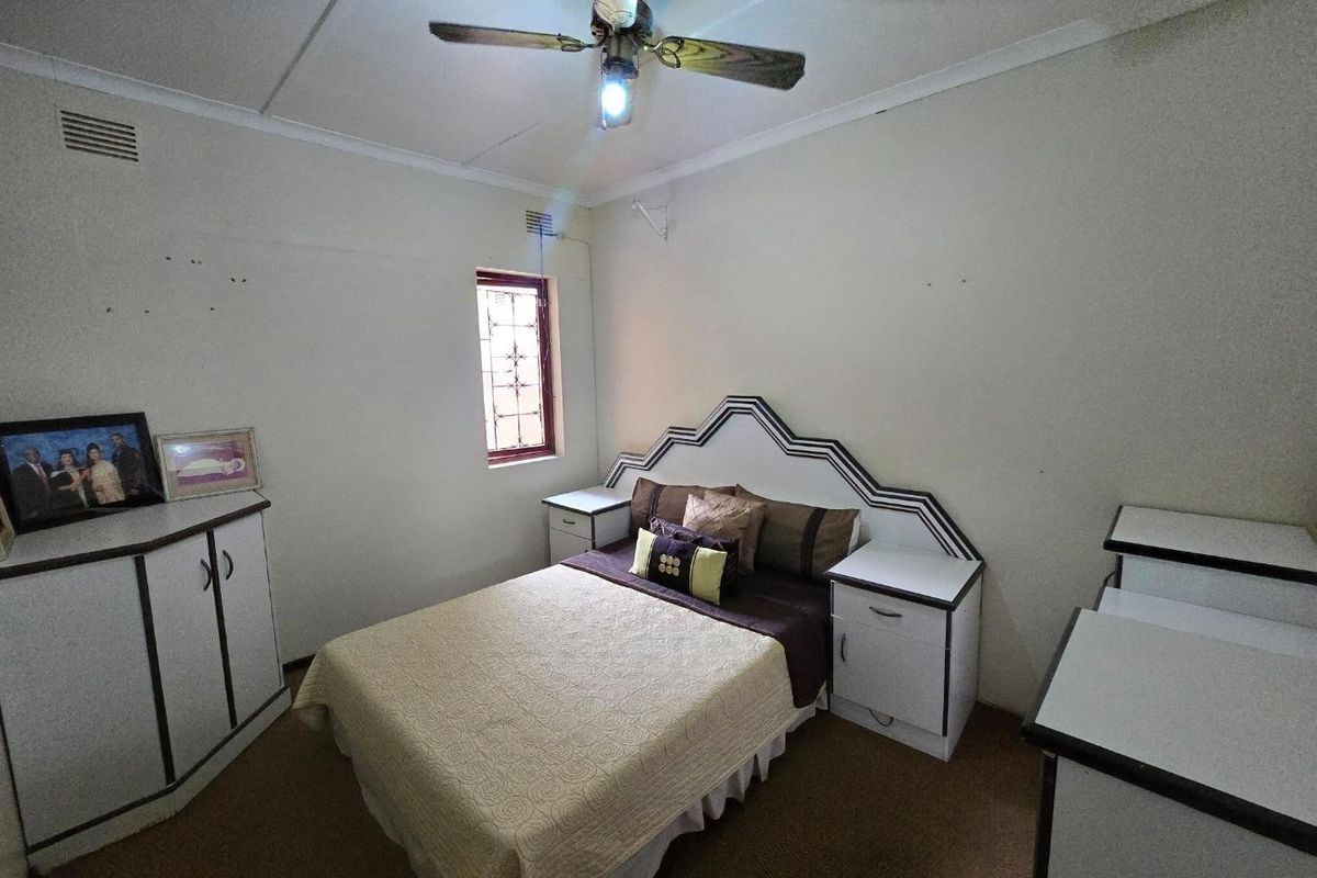 A bedroom featuring built-in cabinetry, a ceiling fan, and security bars on the window. The space requires cosmetic updates to modernize the finishes.