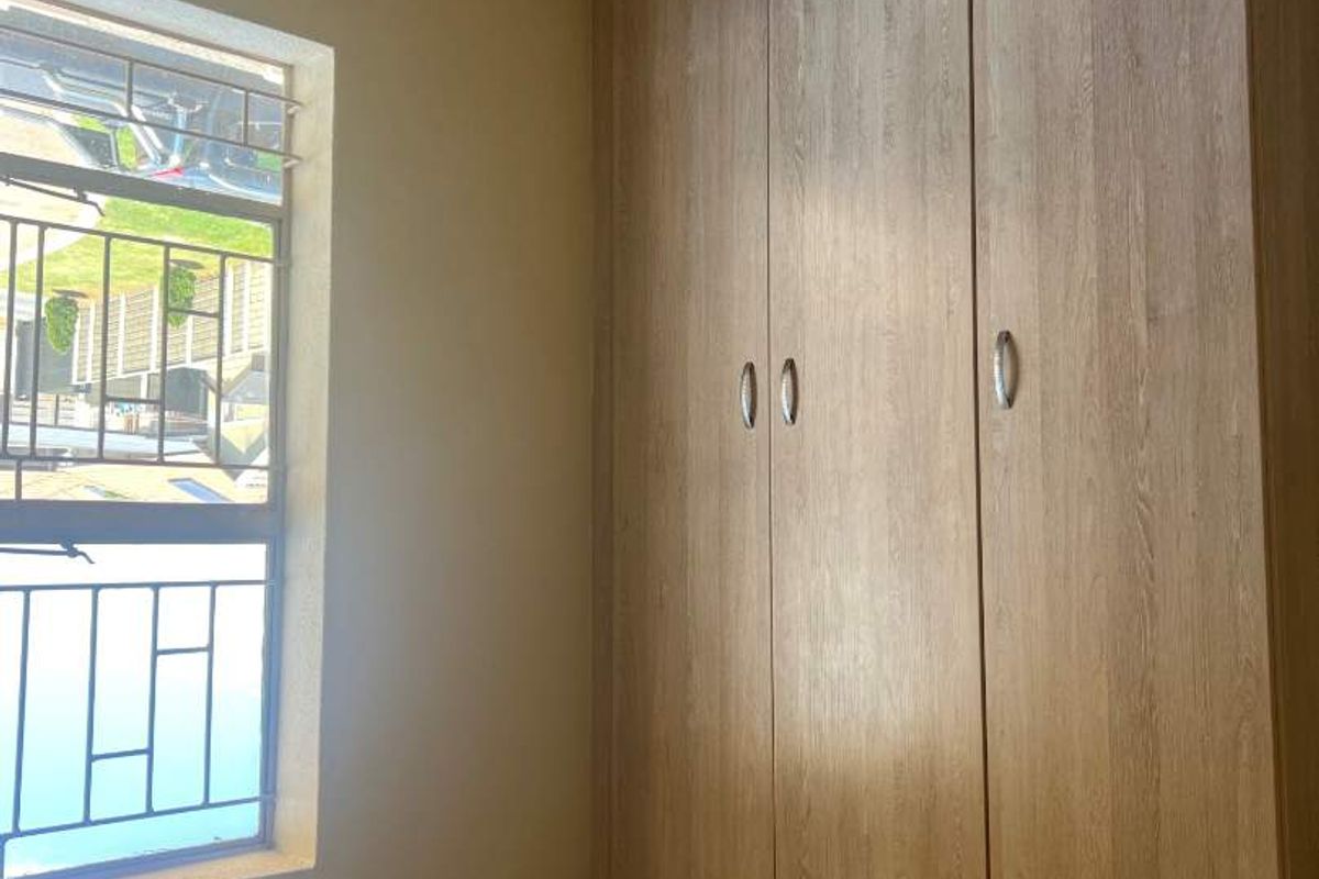 A bedroom featuring built-in wooden cupboards and a window with security bars.