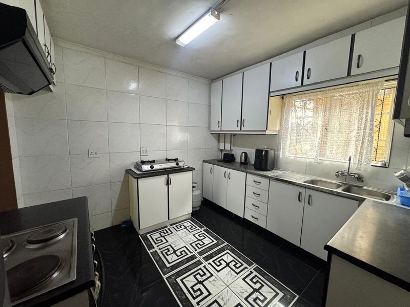 Functional kitchen featuring white built-in cabinetry, tiled splashbacks, a double sink, and integrated hob, offering a practical layout for daily meal preparation.