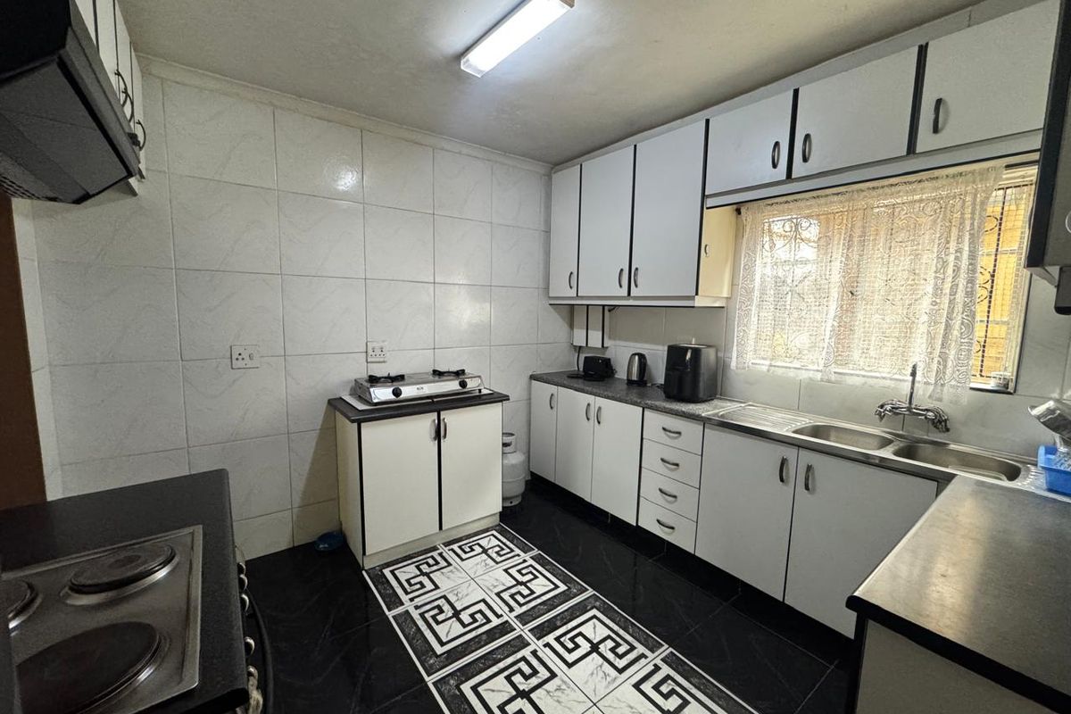 Functional kitchen featuring white built-in cabinetry, tiled splashbacks, a double sink, and integrated hob, offering a practical layout for daily meal preparation.