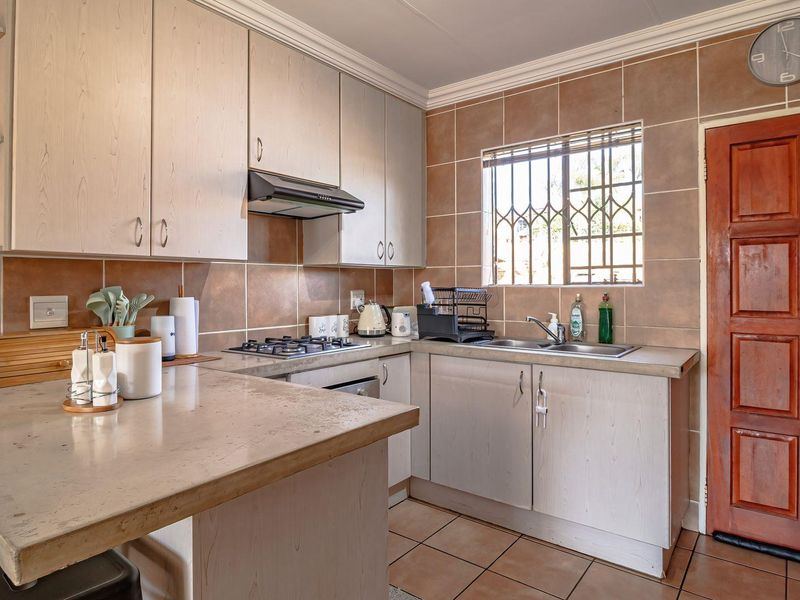 Functional kitchen featuring light-toned built-in cabinetry, gas hob, extractor fan, double sink, and tiled finishes, providing a practical workspace with direct exterior access.