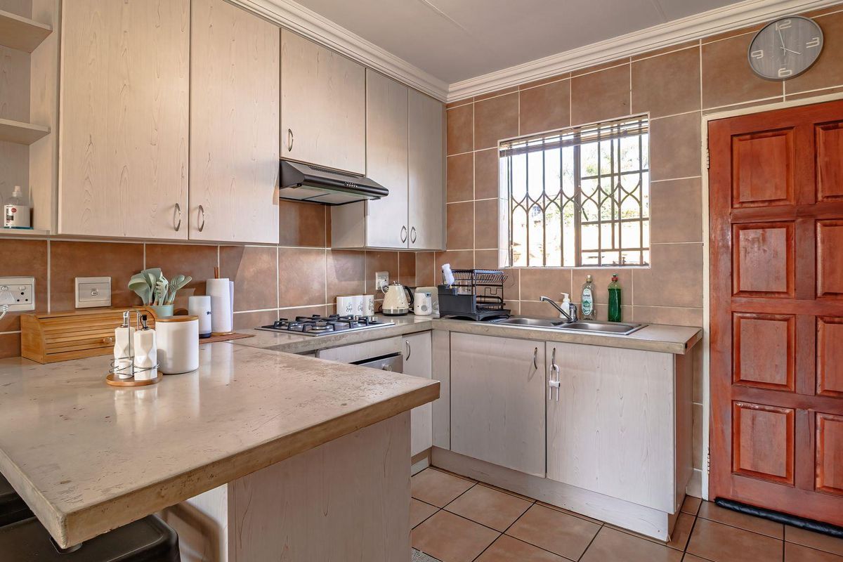 Functional kitchen featuring light-toned built-in cabinetry, gas hob, extractor fan, double sink, and tiled finishes, providing a practical workspace with direct exterior access.