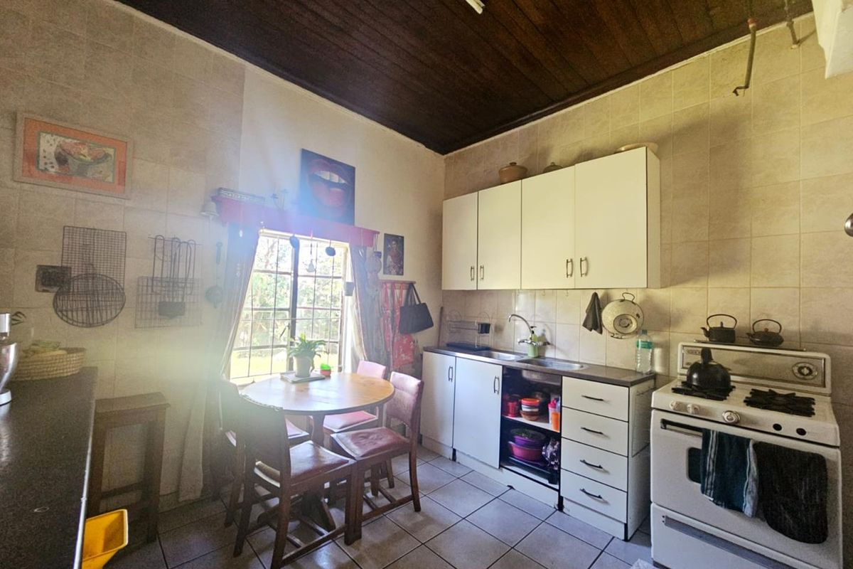 A compact kitchen featuring white cabinetry, tiled walls, a gas stove, and a dark timber ceiling, offering a functional layout with potential for modernization.