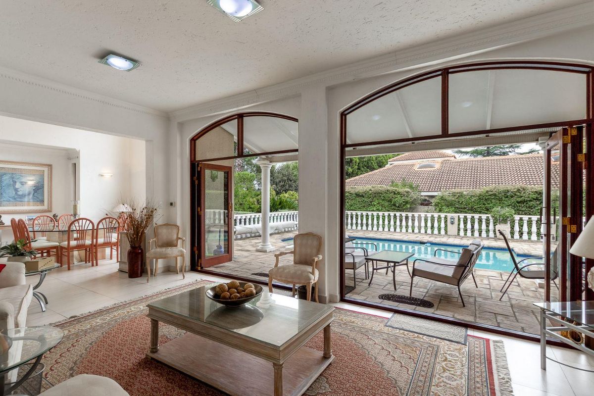 Spacious living area featuring large arched glass doors that open onto a paved patio and swimming pool, creating a seamless indoor-outdoor flow.