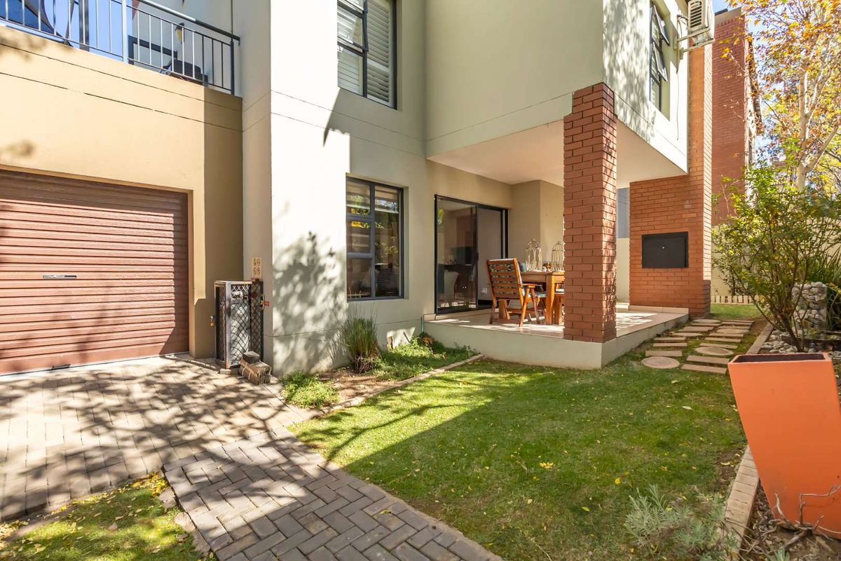 Rear view of the cluster property featuring a covered patio with built-in braai, small garden, paved driveway, and access to the garage.