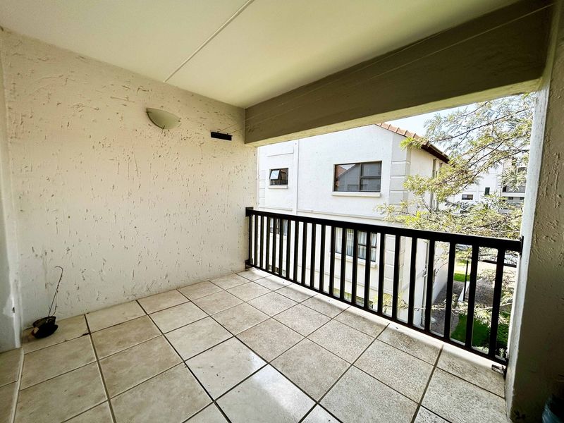 A covered balcony featuring tiled flooring and a metal balustrade, offering an outdoor space with a view of the surrounding apartment complex.