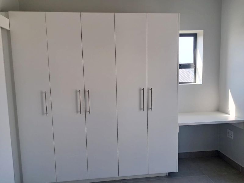 A clean, modern bedroom featuring white built-in cupboards and a matching integrated desk area with tiled flooring.