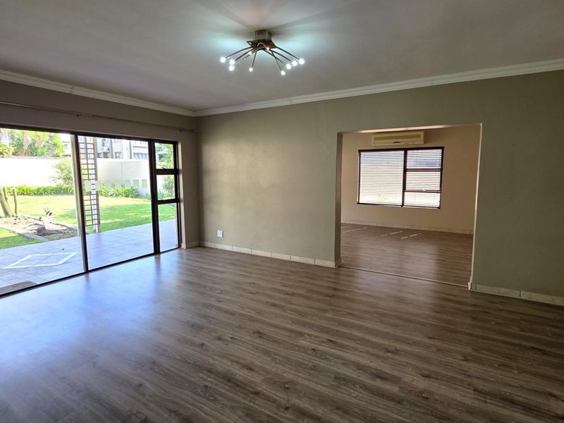 Spacious, light-filled living area featuring modern laminate flooring, large sliding glass doors opening to the garden, and a contemporary chandelier.