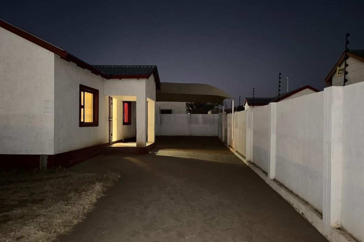 Night view of the property exterior featuring a paved driveway, boundary wall, and covered parking area.