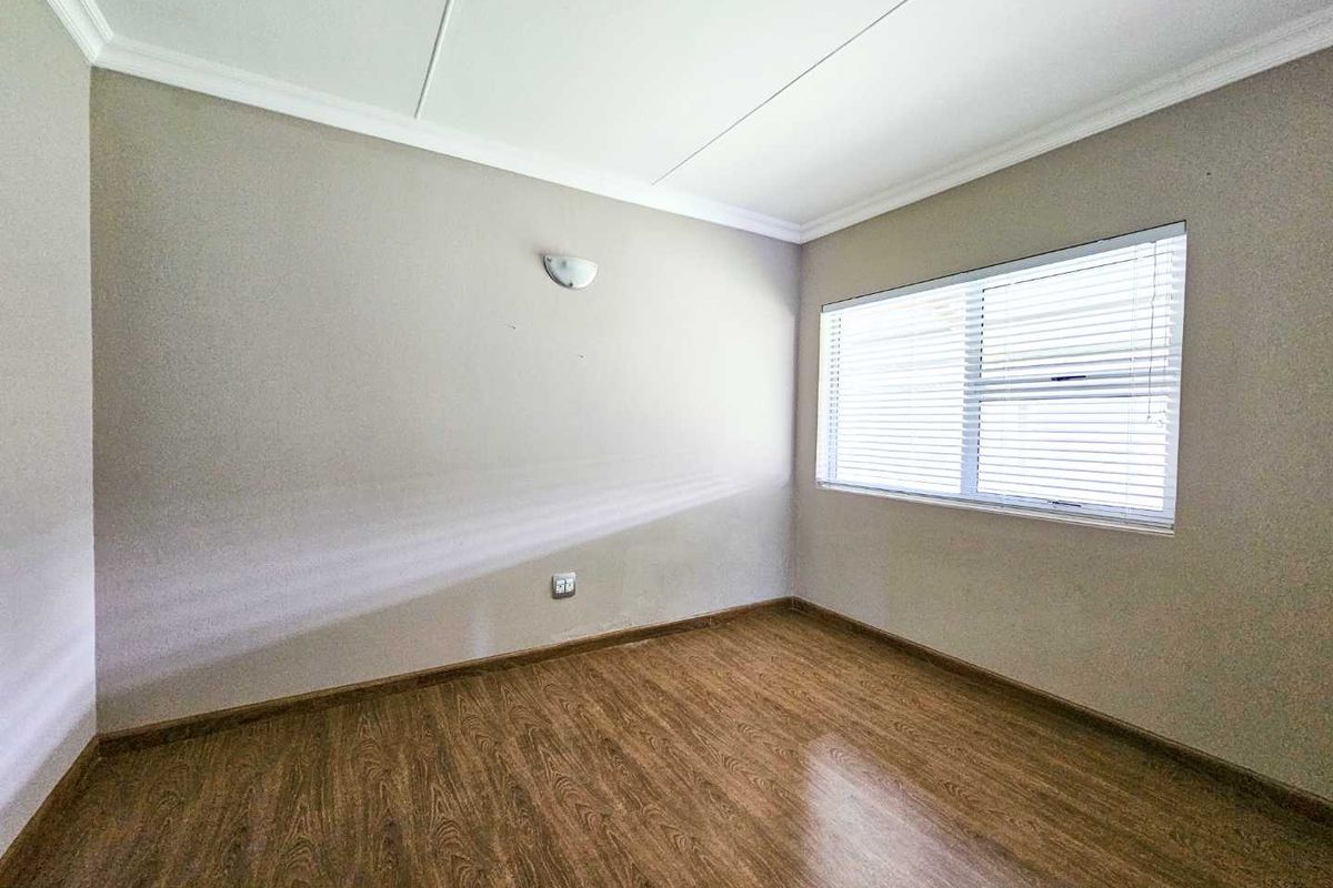 A bright, empty bedroom featuring wood-look laminate flooring, neutral wall tones, and fitted window blinds.