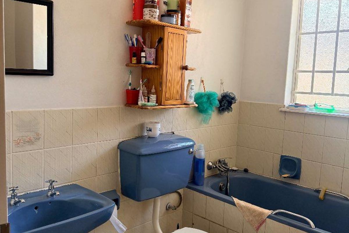 A dated bathroom featuring a blue suite, including a bathtub, toilet, and wall-mounted basin, with tiled walls and a window for natural light.