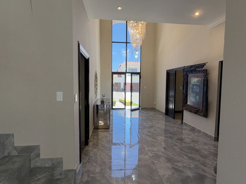 Spacious double-volume entrance hall featuring high ceilings, floor-to-ceiling glass doors, and polished porcelain tile flooring, creating a bright and welcoming atmosphere.