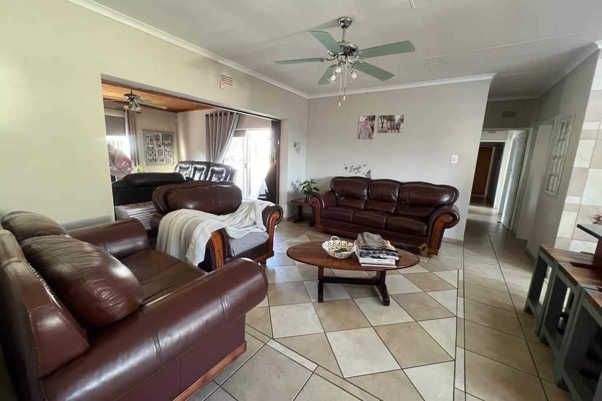 Spacious living room featuring ceramic tile flooring, coved cornicing, and a ceiling fan, with an open-plan flow into the adjacent living area.