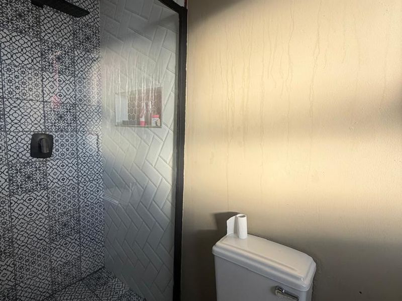 Modern bathroom featuring a walk-in shower with black-framed glass, patterned tiling, and a built-in niche, complemented by a standard toilet.