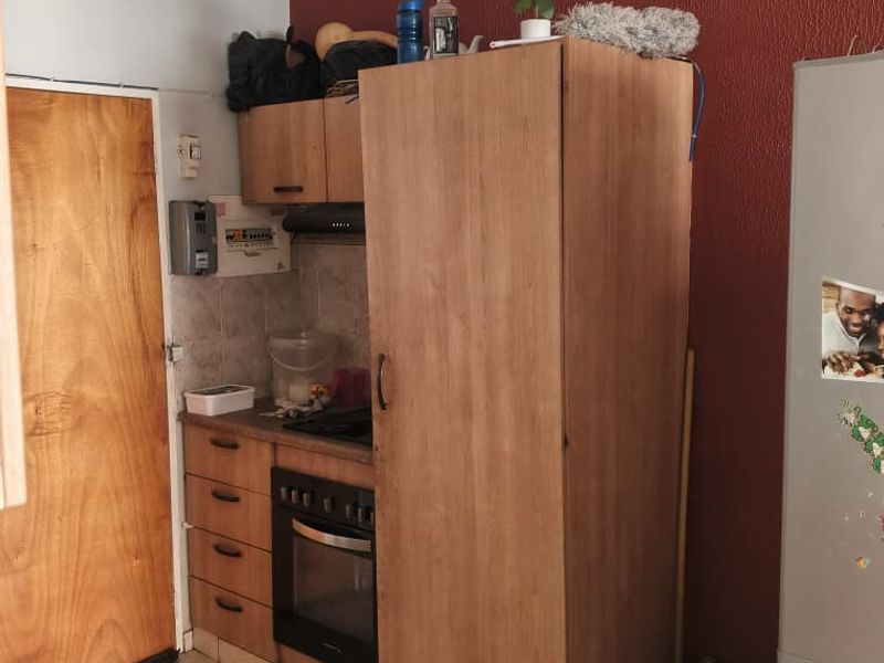Compact kitchen featuring built-in wooden cabinetry, integrated oven, extractor fan, and tiled flooring. The space offers functional storage and preparation areas.
