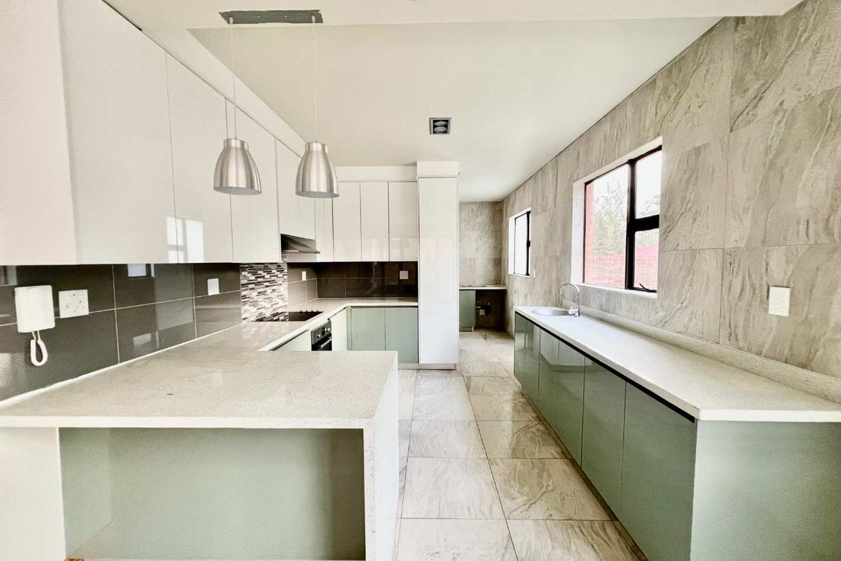Modern kitchen featuring sleek cabinetry, stone countertops, integrated hob and oven, and large format floor tiles in a contemporary, well-lit layout.