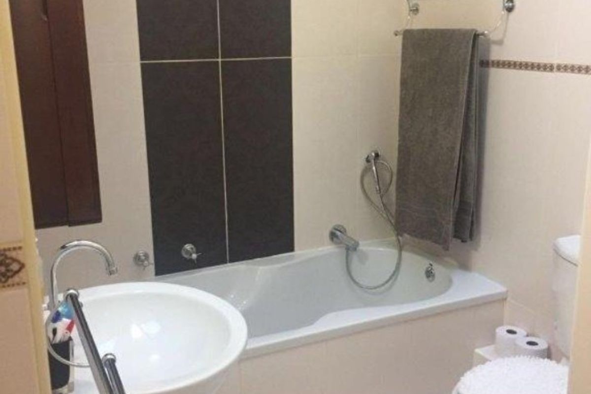 A functional bathroom featuring a pedestal sink, a built-in bathtub with a handheld shower attachment, and a standard toilet with neutral wall and floor tiling.