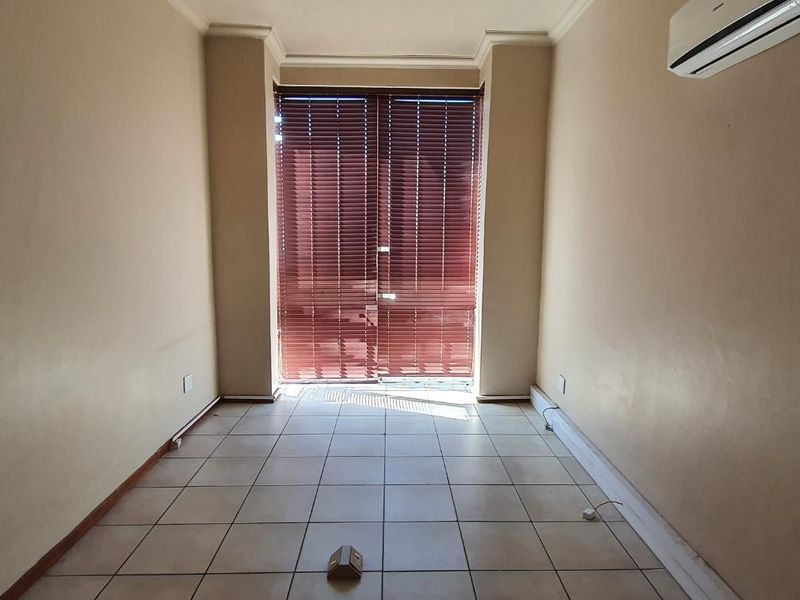 A vacant office space featuring tiled flooring, an integrated air conditioning unit, and sliding glass doors with venetian blinds.