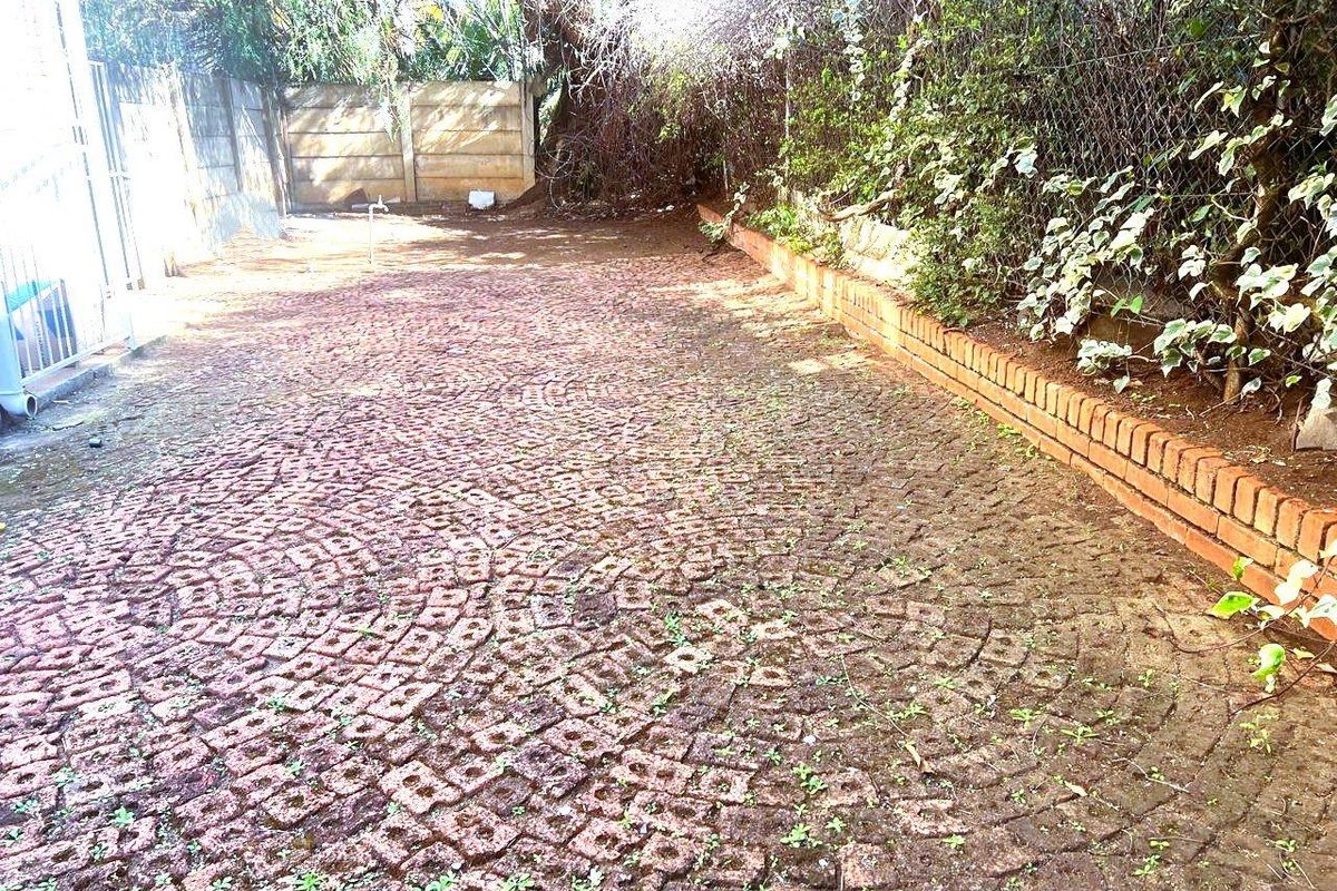 A rear outdoor area featuring cobblestone paving, a brick retaining wall, and perimeter fencing, requiring maintenance and landscaping to improve its overall appeal.