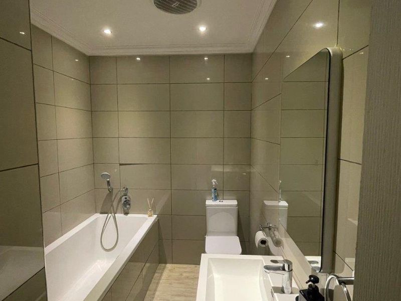 Modern bathroom featuring a built-in bathtub, wall-mounted toilet, and vanity basin with neutral tiled finishes and recessed lighting.