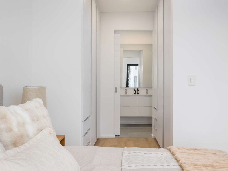 A modern bedroom featuring built-in cupboards and a seamless transition to an en-suite bathroom with a sleek vanity and mirror.