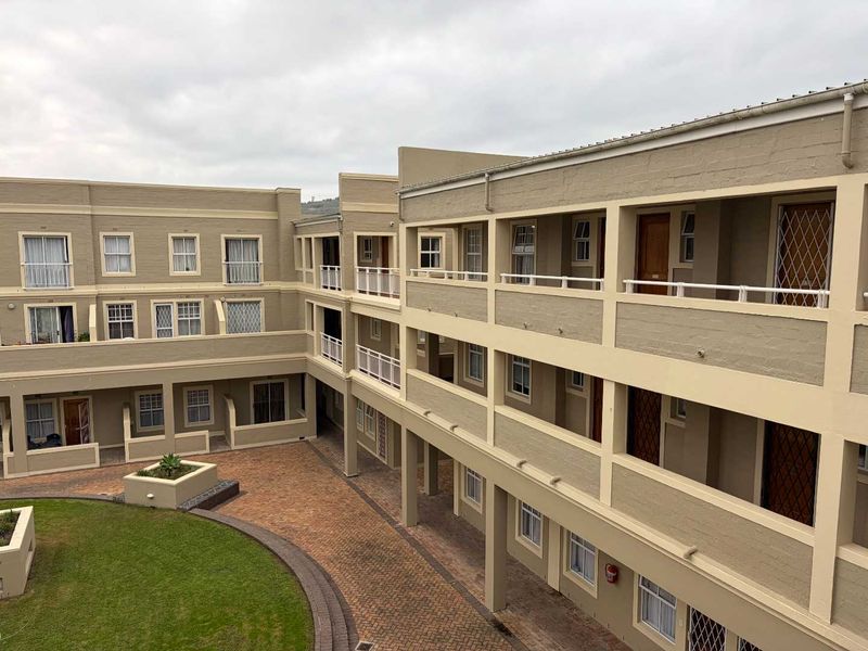 An elevated view of an apartment complex courtyard featuring brick paving, landscaped lawn areas, and multi-story residential units with balcony access.