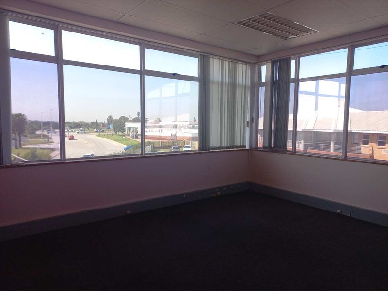 A vacant office space featuring large windows with vertical blinds, carpeted flooring, and a suspended ceiling with recessed lighting.