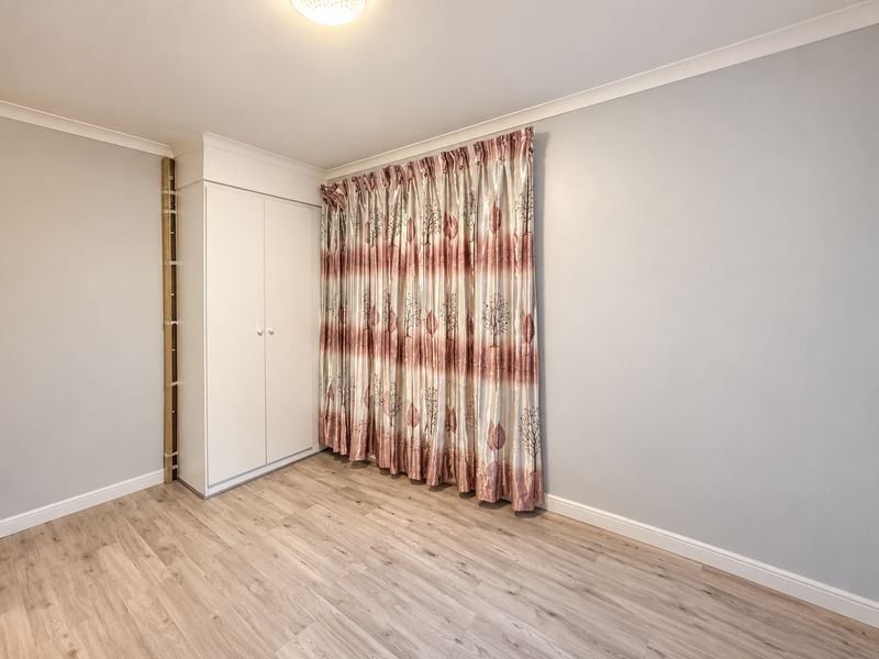 A bright, empty bedroom featuring light laminate flooring, a built-in wardrobe, and neutral wall finishes.