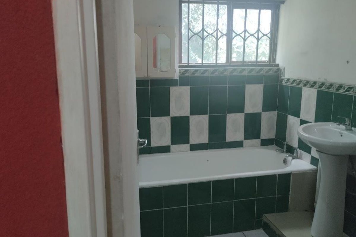 A dated bathroom featuring a bathtub, pedestal basin, and green and white tiled walls with security bars on the window.