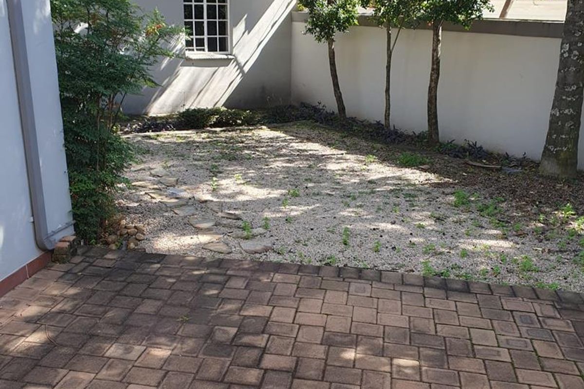 A private rear courtyard featuring paved patio area and a gravel garden section with perimeter boundary walls and mature trees.