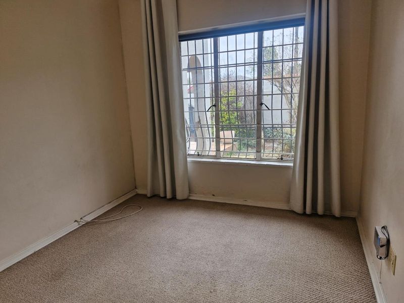 An empty bedroom featuring carpeted flooring and a window fitted with security bars, offering a blank canvas for potential updates.