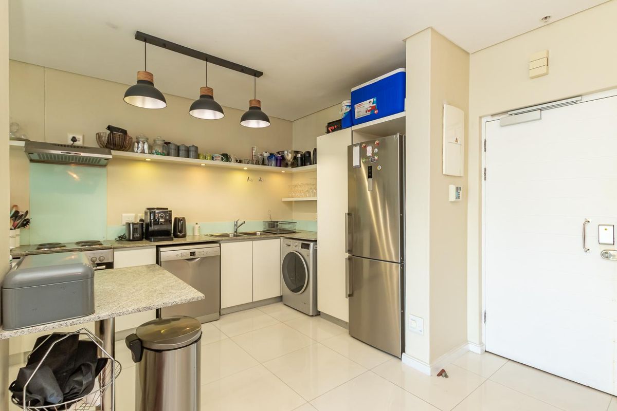 Compact modern kitchen featuring sleek white cabinetry, stone countertops, integrated stainless steel appliances, and contemporary pendant lighting.