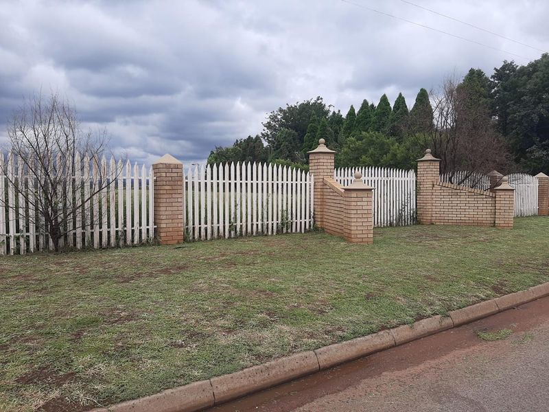 A view of the property boundary featuring a combination of brick pillars and white picket fencing along the street frontage.