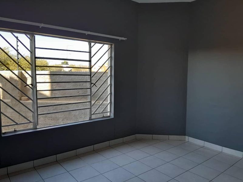 An empty bedroom featuring tiled flooring, dark grey walls, and windows fitted with security bars.