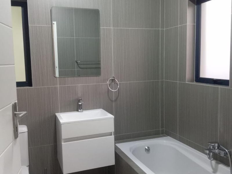 A modern, well-maintained bathroom featuring full-height wall tiling, a wall-mounted vanity with basin, and a bathtub with integrated shower fixtures.