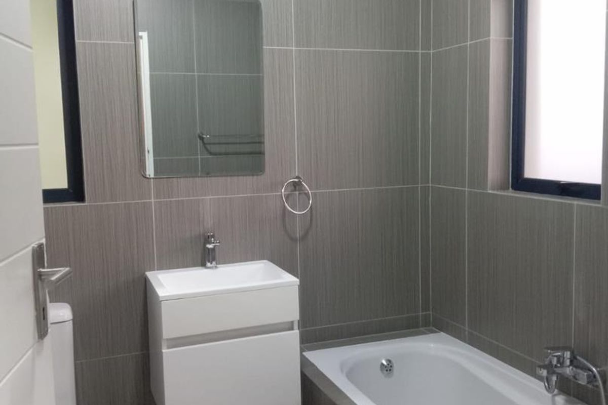 A modern, well-maintained bathroom featuring full-height wall tiling, a wall-mounted vanity with basin, and a bathtub with integrated shower fixtures.