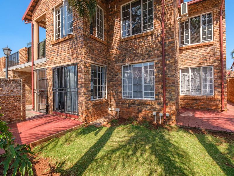 Rear view of a face brick apartment building featuring a paved patio area, small lawn, and secure window and door fittings.