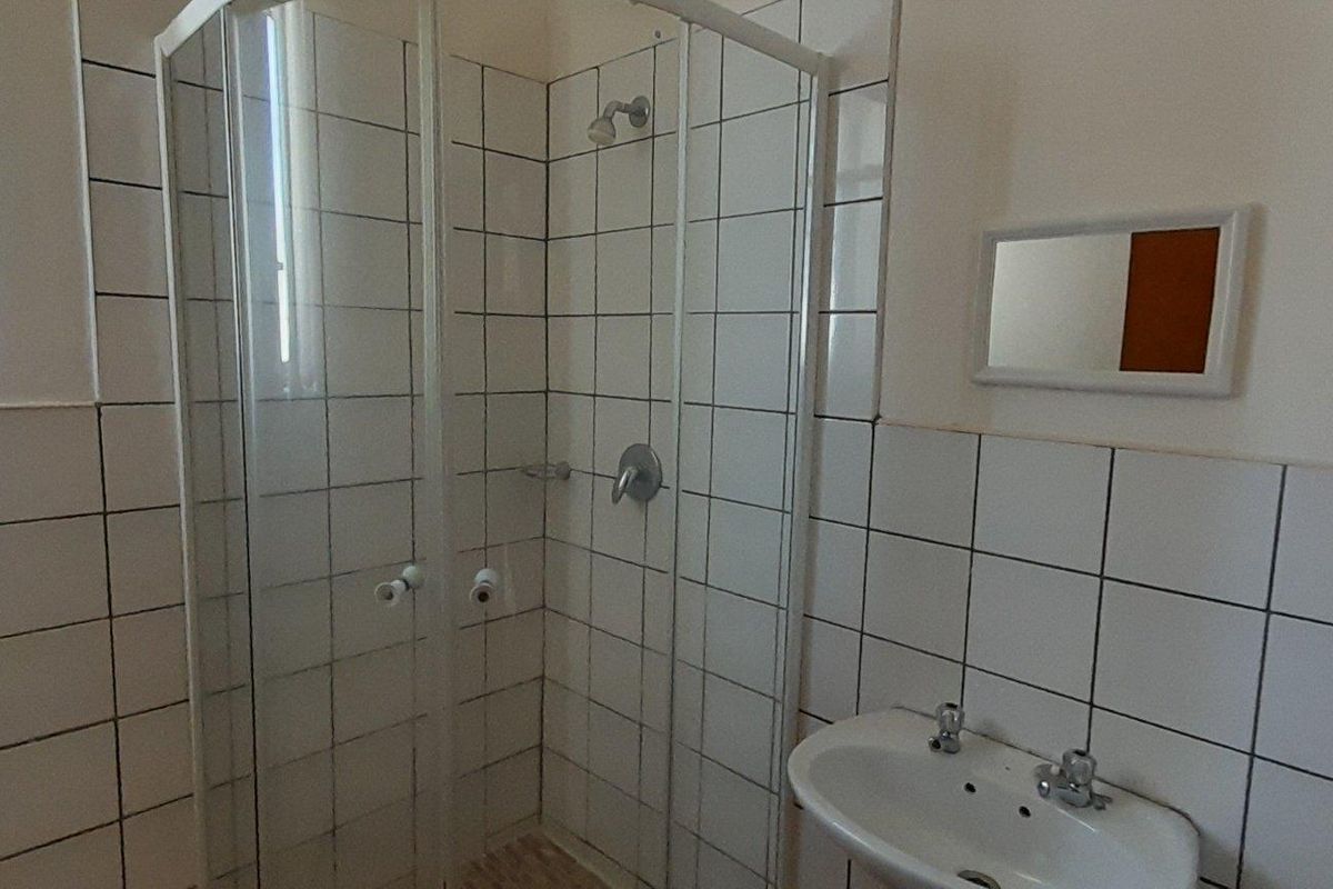 A functional bathroom featuring a corner shower enclosure with white wall tiles and a pedestal basin.