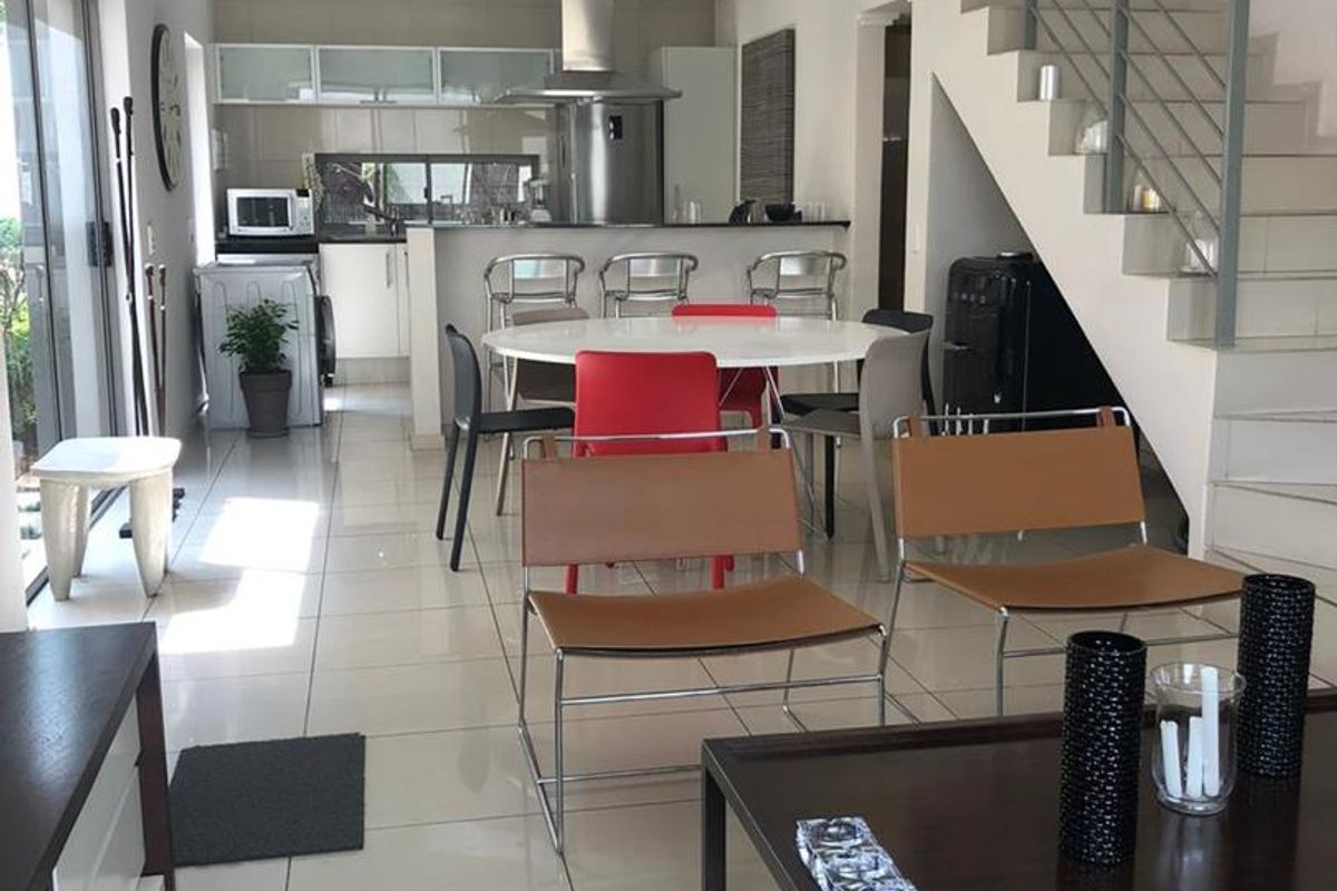 Spacious open-plan living and kitchen area featuring modern tiled floors, a sleek staircase, and direct access to outdoor space through sliding glass doors.
