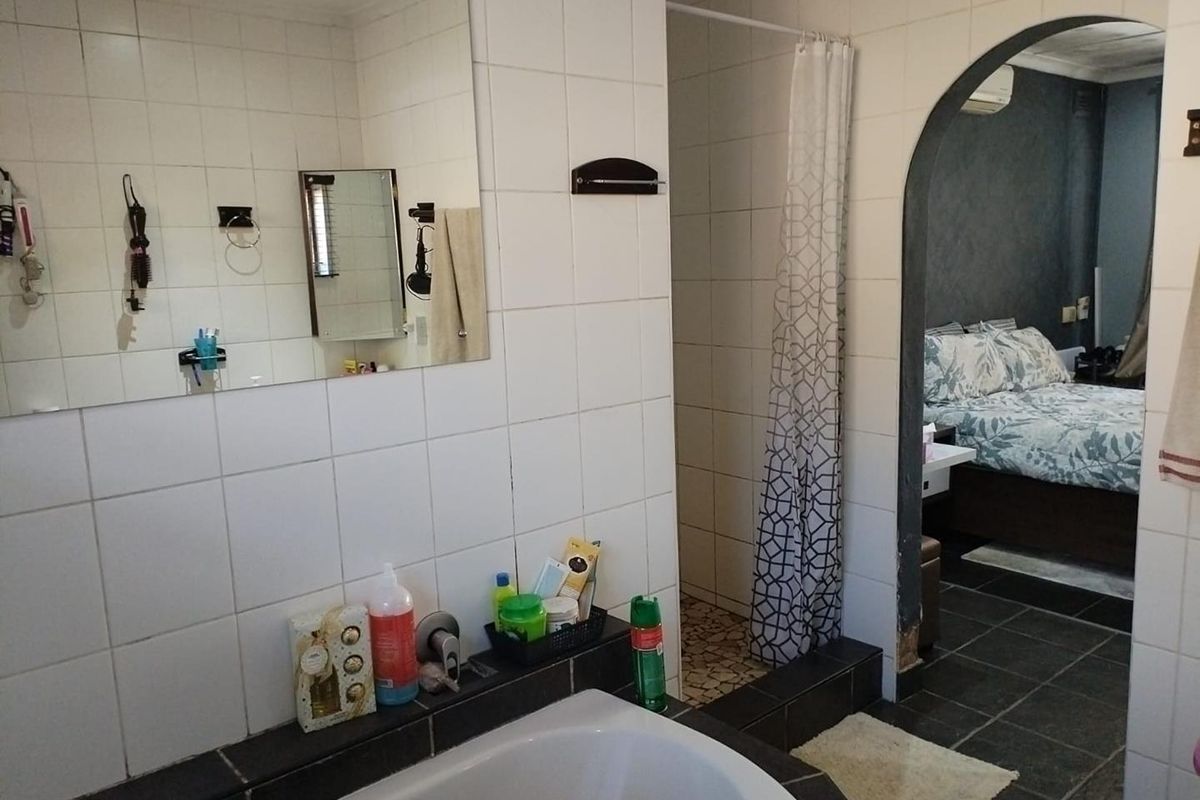 Bathroom featuring a built-in bathtub, wall-mounted mirror, and a shower area with a curtain, leading directly into an adjacent bedroom through an arched doorway.