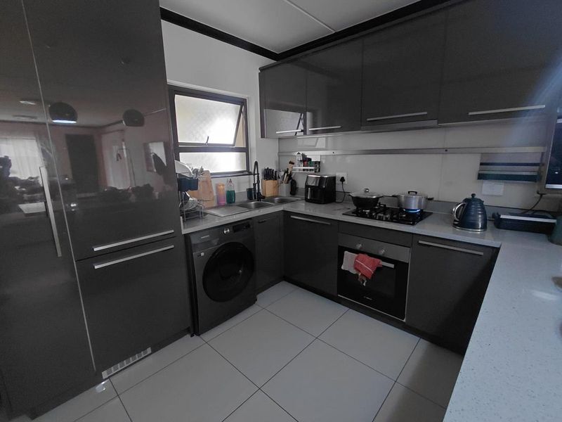 Modern kitchen featuring dark grey cabinetry, stone countertops, integrated washing machine, gas hob, and electric oven with tiled flooring.