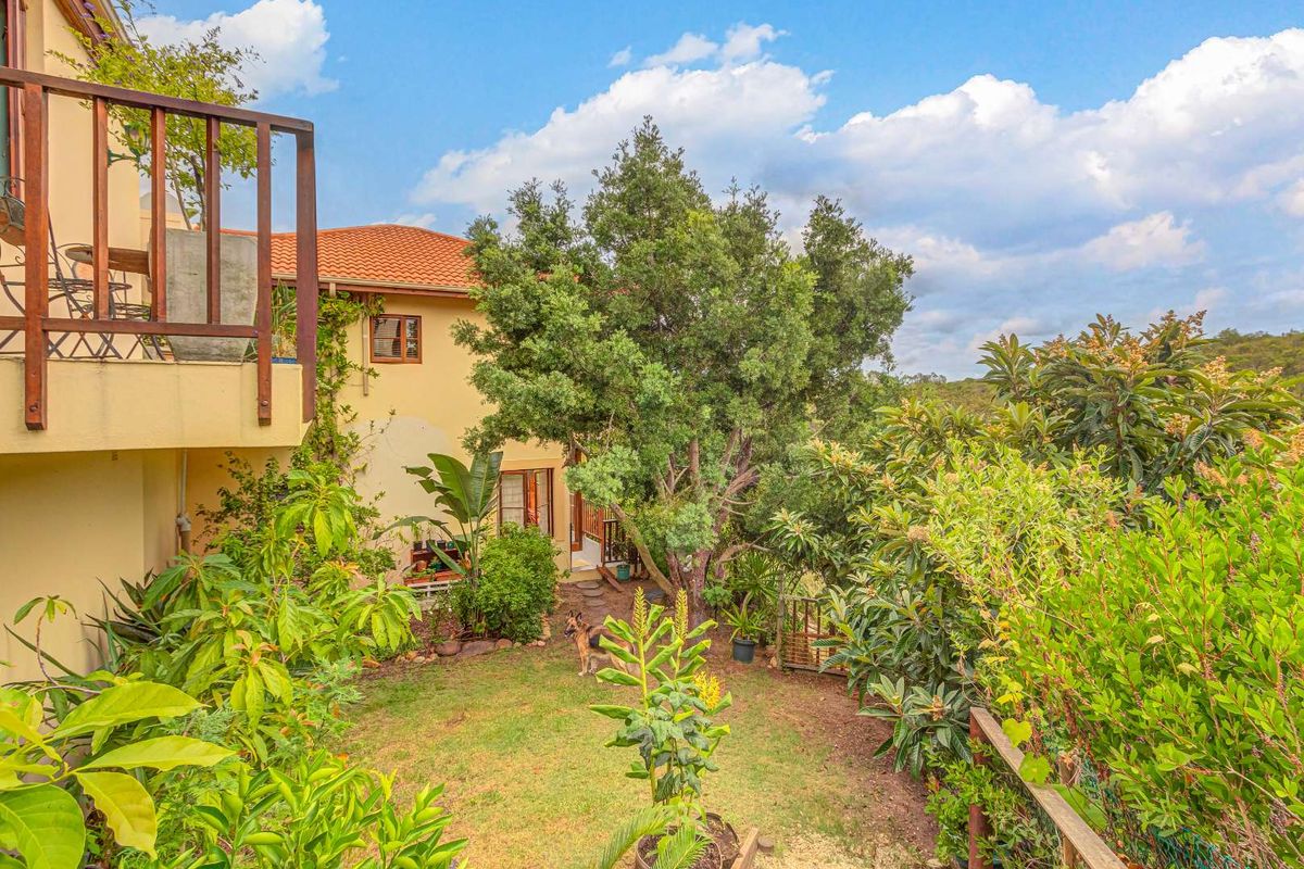 A view of the rear garden and house exterior, featuring a raised timber balcony, lush landscaping, and established trees.