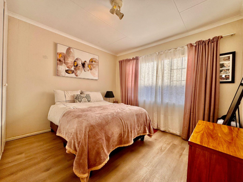 A well-lit bedroom featuring durable laminate flooring, neutral wall finishes, and a built-in cupboard, offering a comfortable and functional living space.