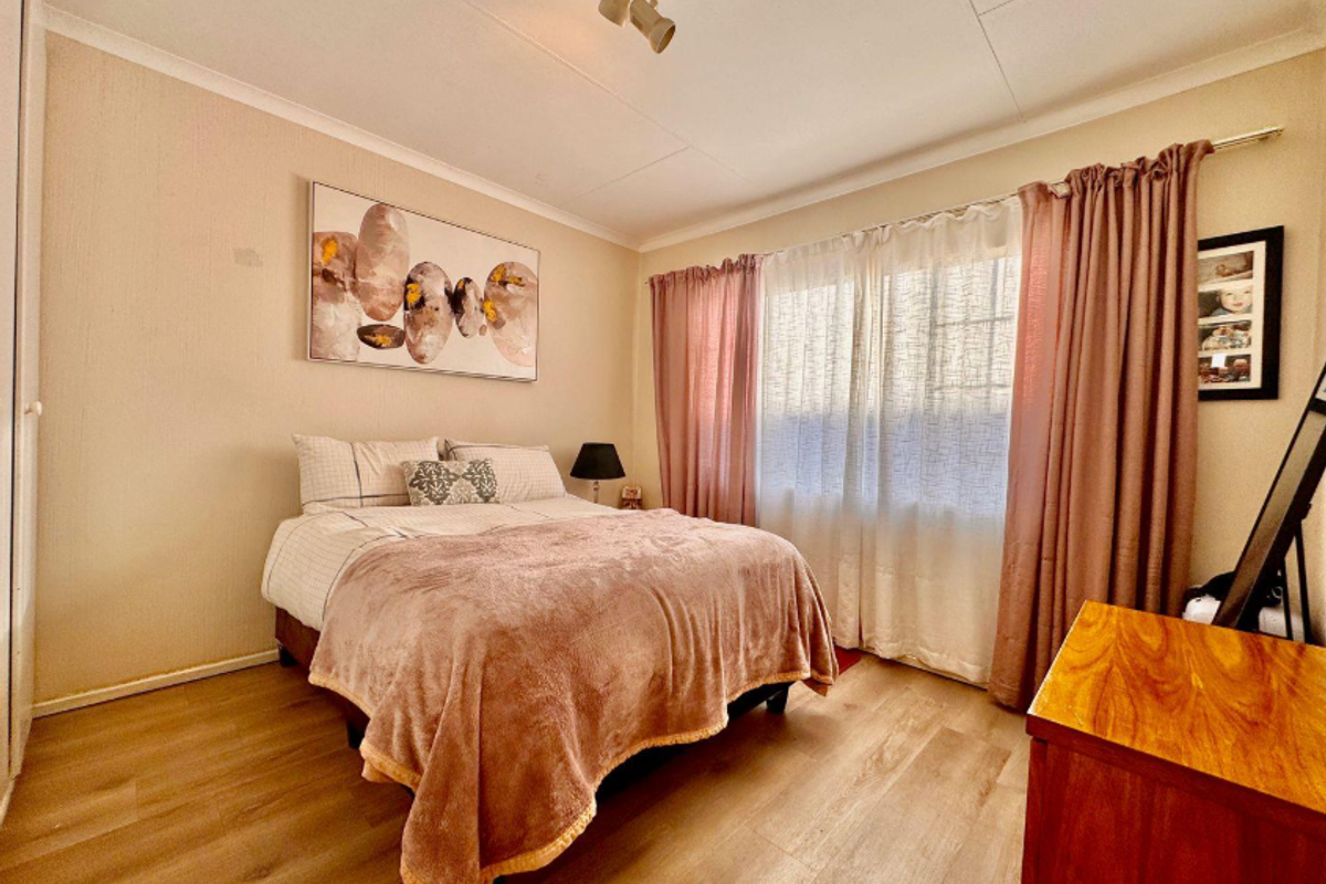 A well-lit bedroom featuring durable laminate flooring, neutral wall finishes, and a built-in cupboard, offering a comfortable and functional living space.