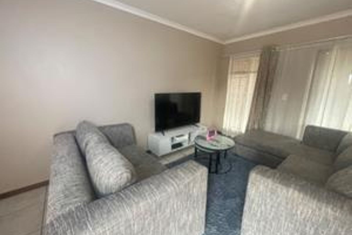 A comfortable living room featuring neutral wall tones, tiled flooring, and large windows with curtain rails, providing a bright and functional space.
