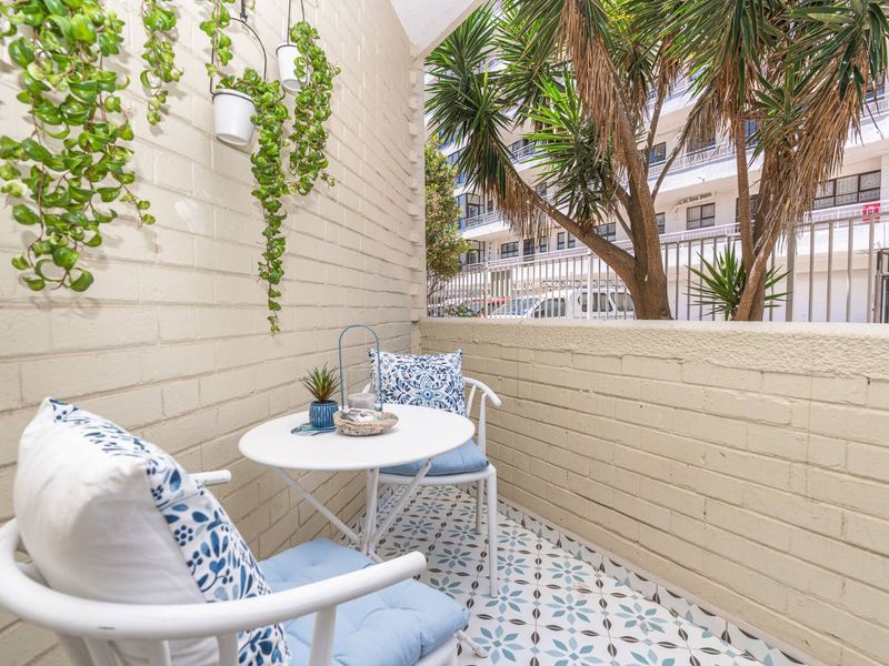 A compact, well-maintained balcony featuring painted brick walls, decorative patterned floor tiles, and a metal balustrade overlooking the surrounding apartment complex.