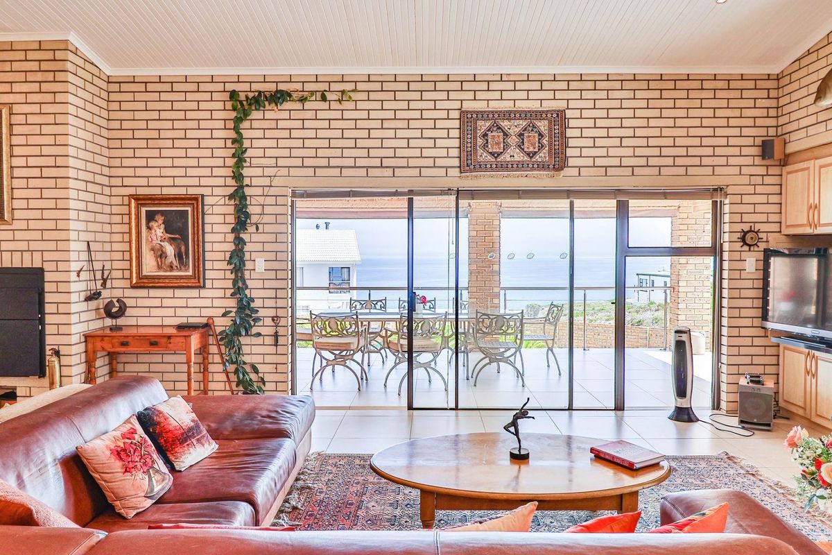 Spacious living room featuring exposed brick walls, tiled flooring, and large sliding glass doors opening onto a covered patio with ocean views.