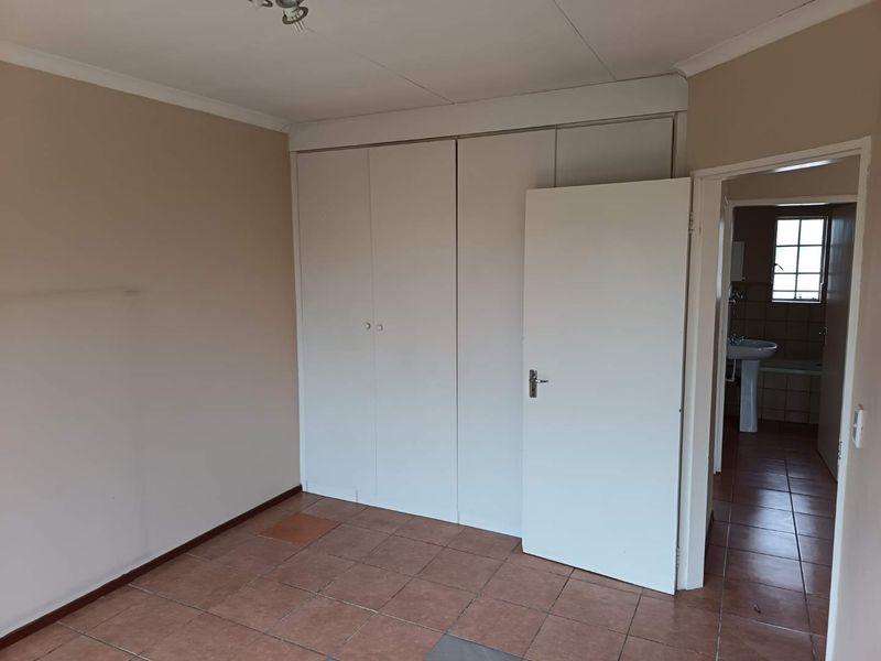 An empty bedroom featuring built-in cupboards and tiled flooring, with an adjacent view into a bathroom area.